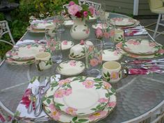 the table is set with plates and cups, silverware and pink flowers on it