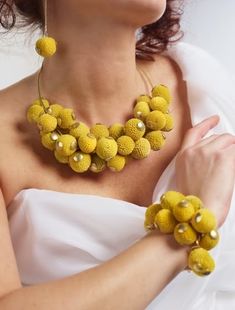 a woman wearing a yellow necklace and matching earrings with her hand on her chest,