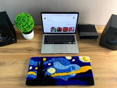 an open laptop computer sitting on top of a wooden desk next to speakers and a potted plant