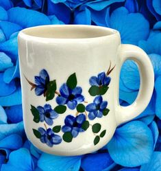 a white coffee cup with blue flowers painted on the side and green leaves around it