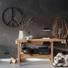 a wooden table sitting in front of a gray wall next to a vase with flowers