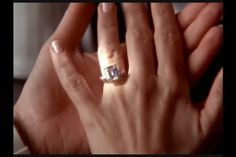 a woman's hand holding an engagement ring in front of her face and the other hand