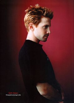 a man standing in front of a red wall with his hand on his hip and looking off to the side