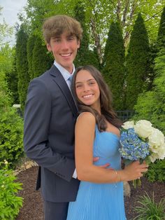 a young man and woman in formal wear posing for a photo together, with flowers in the foreground