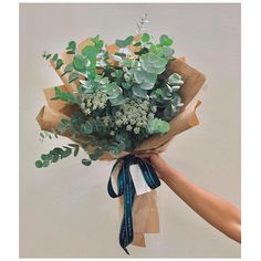 a person holding a bouquet of flowers with green leaves and blue ribbon tied around it