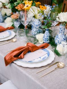 the table is set with blue and white china plates, silverware, and flowers