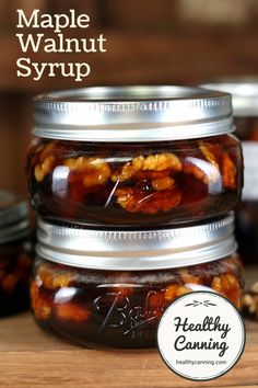 three jars filled with maple walnut syrup sitting on top of a wooden table next to nuts