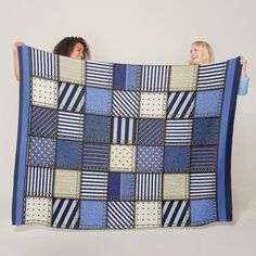 two women are holding up a blue and white patchwork blanket that has squares on it