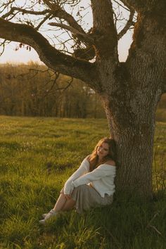 a woman sitting under a tree in the grass