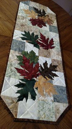 a quilted table runner with autumn leaves on it's sides and the center