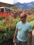 a man is standing in front of some flowers and bushes with sunglasses on his face