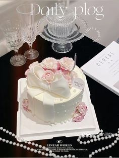 there is a cake on the table with pink flowers and pearls next to wine glasses