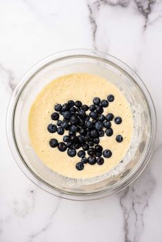 a glass bowl filled with batter and blueberries on top of a white marble counter