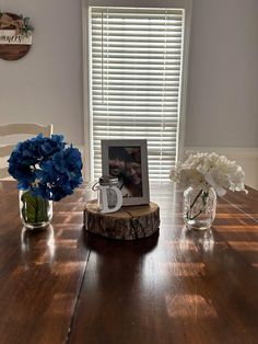 a wooden table topped with vases filled with flowers next to a window covered in blinds