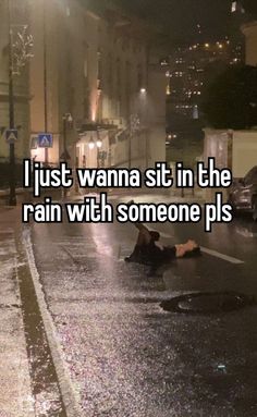 a person laying on the ground in the rain next to a street with cars and buildings