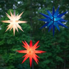 three star shaped lights hanging from strings in front of trees