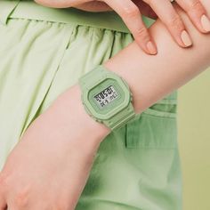 a close up of a person with a watch on their wrist and green dress behind her