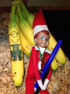 an elf is standing next to bananas on the counter with a blue pen in his hand