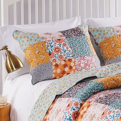 a bed with colorful pillows on top of it and a gold lamp next to it