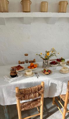 a white table topped with plates and bowls filled with food next to two wooden chairs