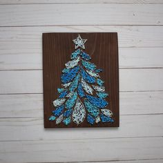 a wooden plaque with a blue and white christmas tree on it's side, against a white wood background