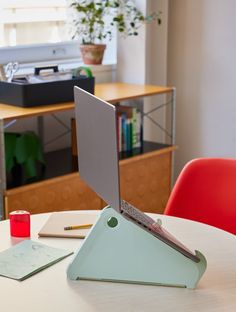 an open laptop computer sitting on top of a white table next to a red chair