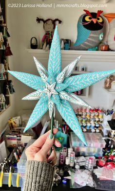 a person holding up a paper star in front of a shelf full of other items