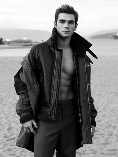 a man standing on top of a sandy beach next to the ocean wearing a jacket