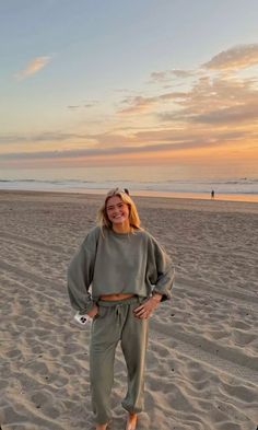 a woman standing on top of a sandy beach next to the ocean with her hands in her pockets