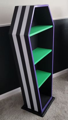 a black and white book shelf with green shelves on the bottom, in front of a black wall