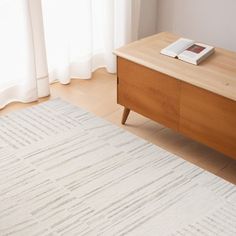 a white rug on the floor in front of a wooden dresser with a book on it