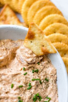 a white bowl filled with dip and crackers next to chips on the side,