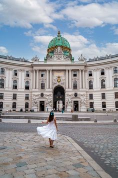 a woman in a white dress is walking towards a large building with a green dome