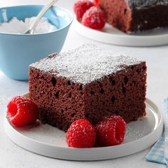 a piece of chocolate cake on a plate with raspberries and powdered sugar