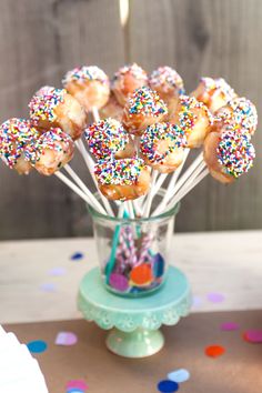 sprinkle covered donuts in a glass vase on a table with confetti sticks