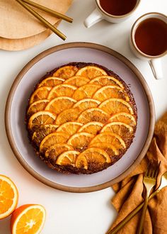 an orange upside down cake on a plate next to two cups of tea and cinnamon sticks