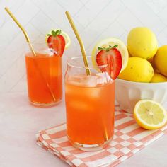 two glasses filled with lemonade and strawberries on top of a checkered cloth