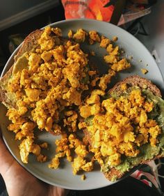 a person holding a plate with eggs and toast on it in front of some books