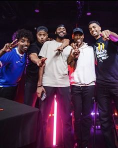 four young men posing for the camera in front of a purple and black backdrop with lights