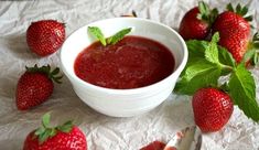 some strawberries are next to a small bowl of strawberry jam on a white tablecloth