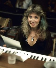 a woman sitting in front of a keyboard with an instrument on her lap and another person standing next to her