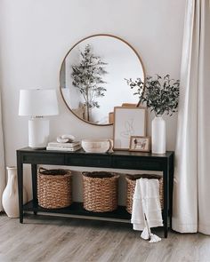 a black console table with two baskets and a round mirror above it on the wall