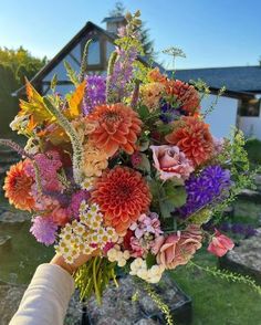 a bouquet of flowers is being held up by someone's hand in front of a house