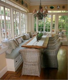 a dining room table with chairs and a bench in front of the window, surrounded by windows