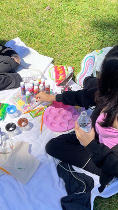 a woman sitting on top of a white blanket holding a water bottle and painting supplies