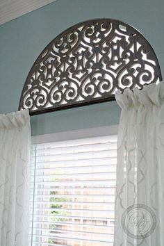 an arched window with white curtains in front of it and a curtain valance over the window