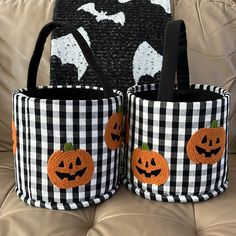 two black and white baskets with pumpkins on them sitting on a couch next to each other