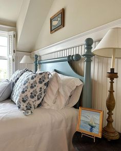 a bed with white sheets and blue headboard next to a painting on the wall