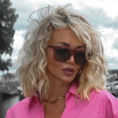 a woman with blonde hair and sunglasses looking off to the side while wearing a pink shirt