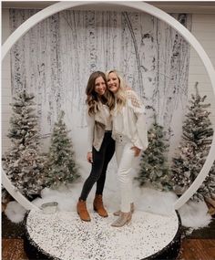 two women standing in front of a snow globe with christmas trees and pine trees behind them